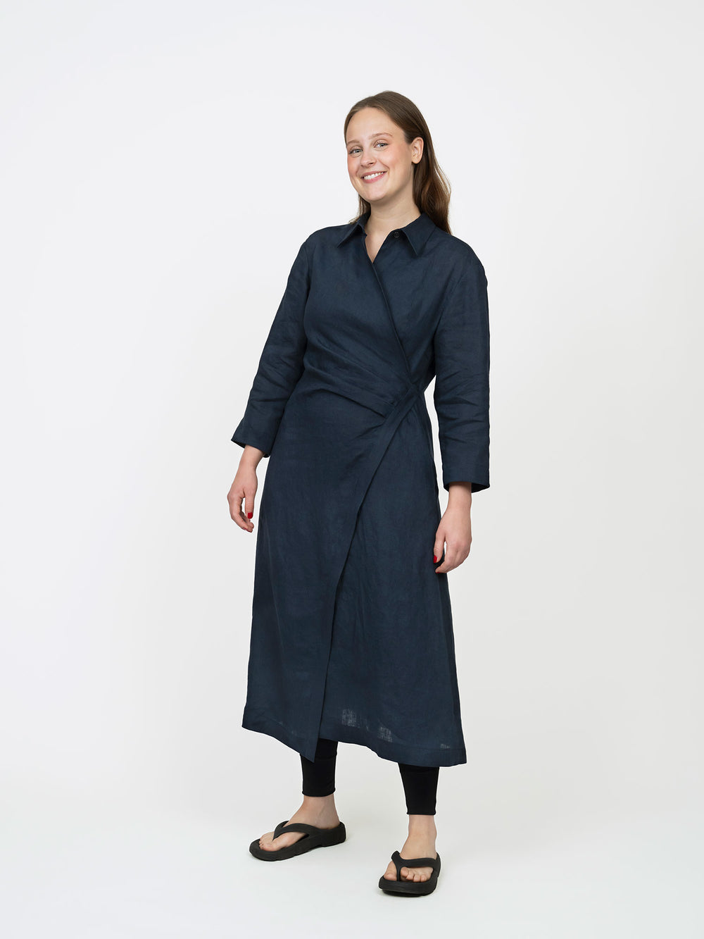 Woman wearing the Wrap Dress sewing pattern from The Assembly Line on The Fold Line. A dress pattern made in light to medium weight fabric, featuring a shirt collar, bracelet-length sleeves, single button fastening on one side, asymmetrical A-line skirt, pockets, and midi length.