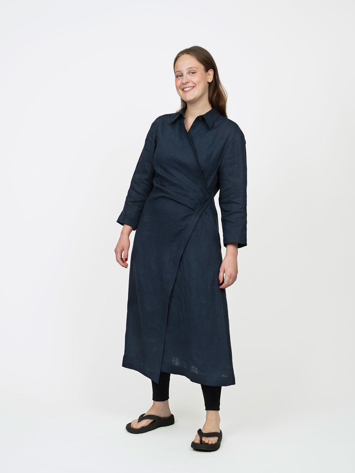 Woman wearing the Wrap Dress sewing pattern from The Assembly Line on The Fold Line. A dress pattern made in light to medium weight fabric, featuring a shirt collar, bracelet-length sleeves, single button fastening on one side, asymmetrical A-line skirt, pockets, and midi length.