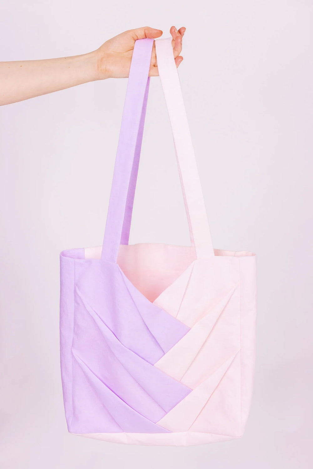Person holding the Xenta Tote Bag sewing pattern from Forget-me-not Patterns on The Fold Line. A tote bag pattern made in medium weight woven fabric, featuring interlocking box pleats, side gussets, an internal pocket, and lining.
