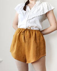 Woman wearing the Yarrow Shorts sewing pattern from Oh Me Oh My Sewing on The Fold Line. A shorts pattern made in quilting cotton, washed linen, viscose, cotton lawn, voile, or rayon challis fabric, featuring a breezy fit, high elasticated waist, faux drawstring, pockets, and stylish curved hem.