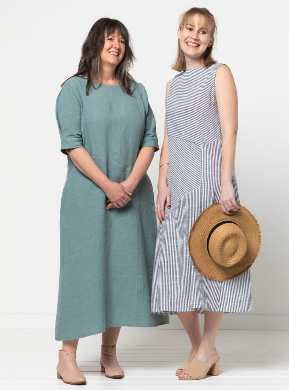 Women wearing the Yvette Woven Dress sewing pattern from Style Arc on The Fold Line. A dress pattern made in linen, crepe, rayon, or cotton fabric, featuring an A-line shape, boat neck, panelled asymmetrical design lines, sleeveless or elbow length sleeves, and midi length.