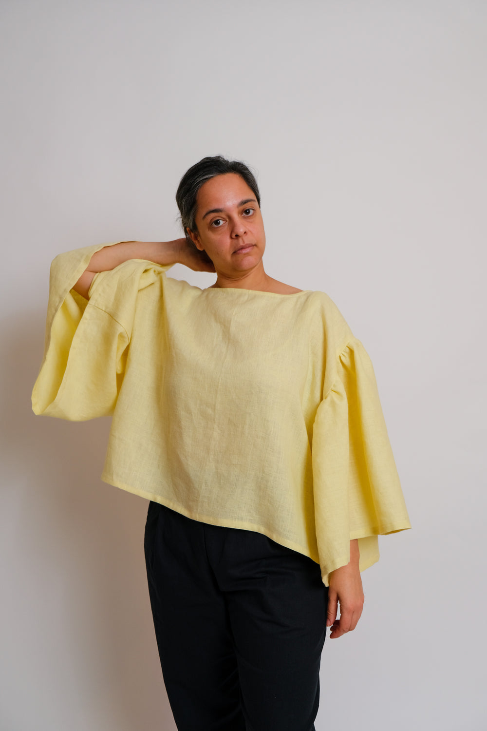 Woman wearing the ZW Frill Sleeve Top sewing pattern from Birgitta Helmersson on The Fold Line. A top pattern made in lightweight cotton or linen fabric, featuring an oversized fit, boat neck, side splits, and voluminous gathered sleeves.