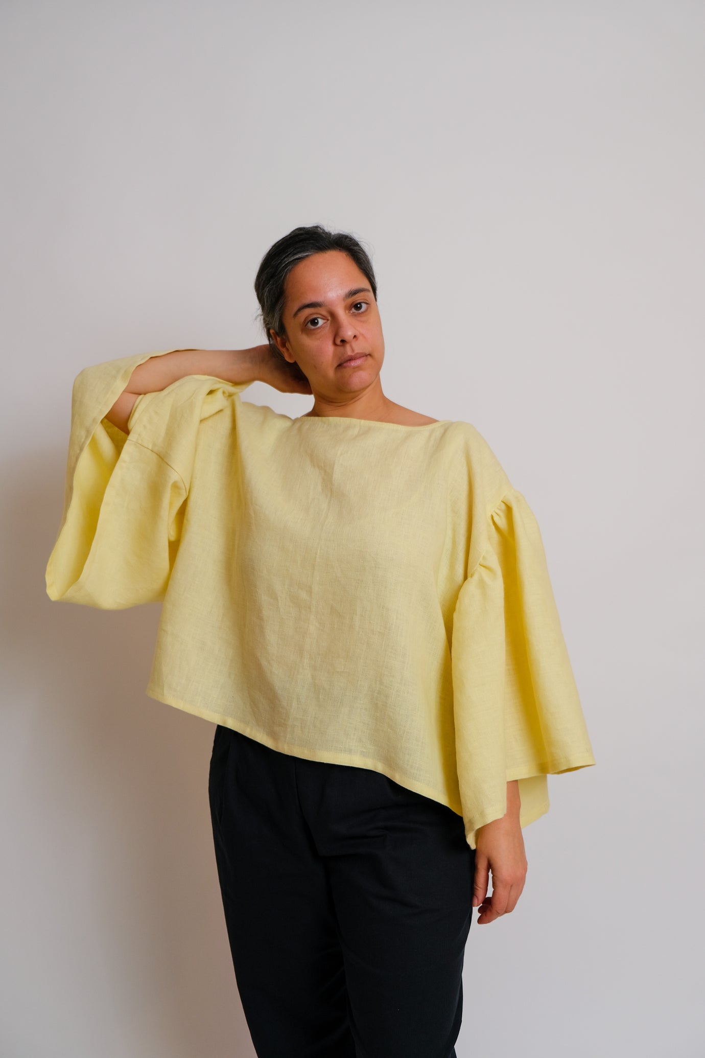 Woman wearing the ZW Frill Sleeve Top sewing pattern from Birgitta Helmersson on The Fold Line. A top pattern made in lightweight cotton or linen fabric, featuring an oversized fit, boat neck, side splits, and voluminous gathered sleeves.