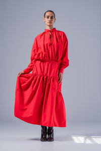 Woman wearing the Zafira Dress sewing pattern from Fibre Mood on The Fold Line. A dress pattern made in poplin or leather fabric, featuring a high collar with a tie, blouson bodice, long sleeves with cuffs, tiered gathered skirt, and maxi length.
