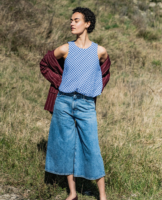 Woman wearing the Zen Top sewing pattern from Fibre Mood on The Fold Line. A sleeveless top pattern made in poplin, cotton satin, linen, nylon, taffeta, crepe, viscose, chambray, seersucker, lyocell, or double gauze fabric, featuring a round neckline, buttons at the back, and balloon hem.
