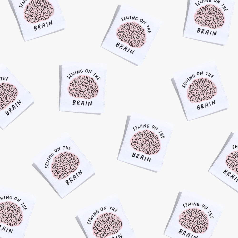 Photo showing 'Sewing on the Brain' Labels from Kylie & The Machine on The Fold Line. A washable, durable, and non-scratchy label. Included are, 6 woven labels showing a brain with black writing on a white background. They are all ready to be sewn into yo