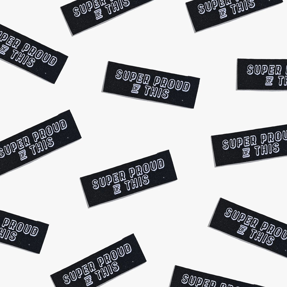 Photo showing 'Super Proud of This' Labels from Kylie & The Machine on The Fold Line. A washable, durable, and non-scratchy label. Included are, 6 woven labels with white writing on a black background. They are all ready to be sewn into your handmade clot