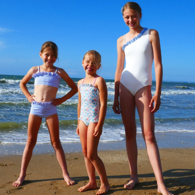 Children wearing the Child/Teen Calella Swimsuit sewing pattern from Petits D’om on The Fold Line. A swimsuit/bikini pattern made in lycra for swimwear fabrics, featuring a one-piece version with a broad shoulder strap and frill plus a spaghetti strap, or