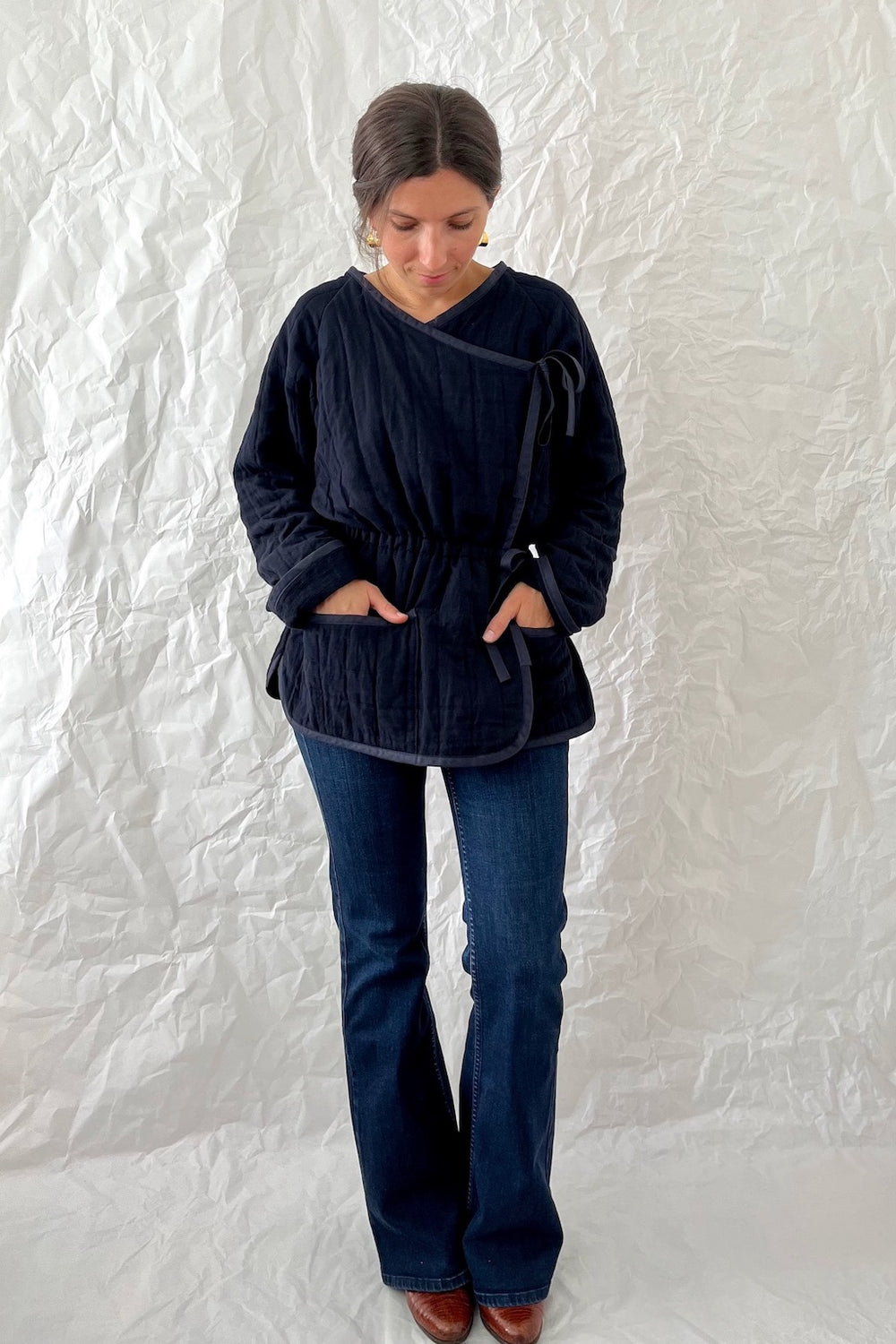 Woman wearing the Coquillage Quilted Jacket sewing pattern from Camimade on The Fold Line. A quilted jacket pattern made in pre-quilted fabrics, featuring a wrap style, elasticated waist, bias tape waist and necktie, V-neck, turned back long sleeves, two 