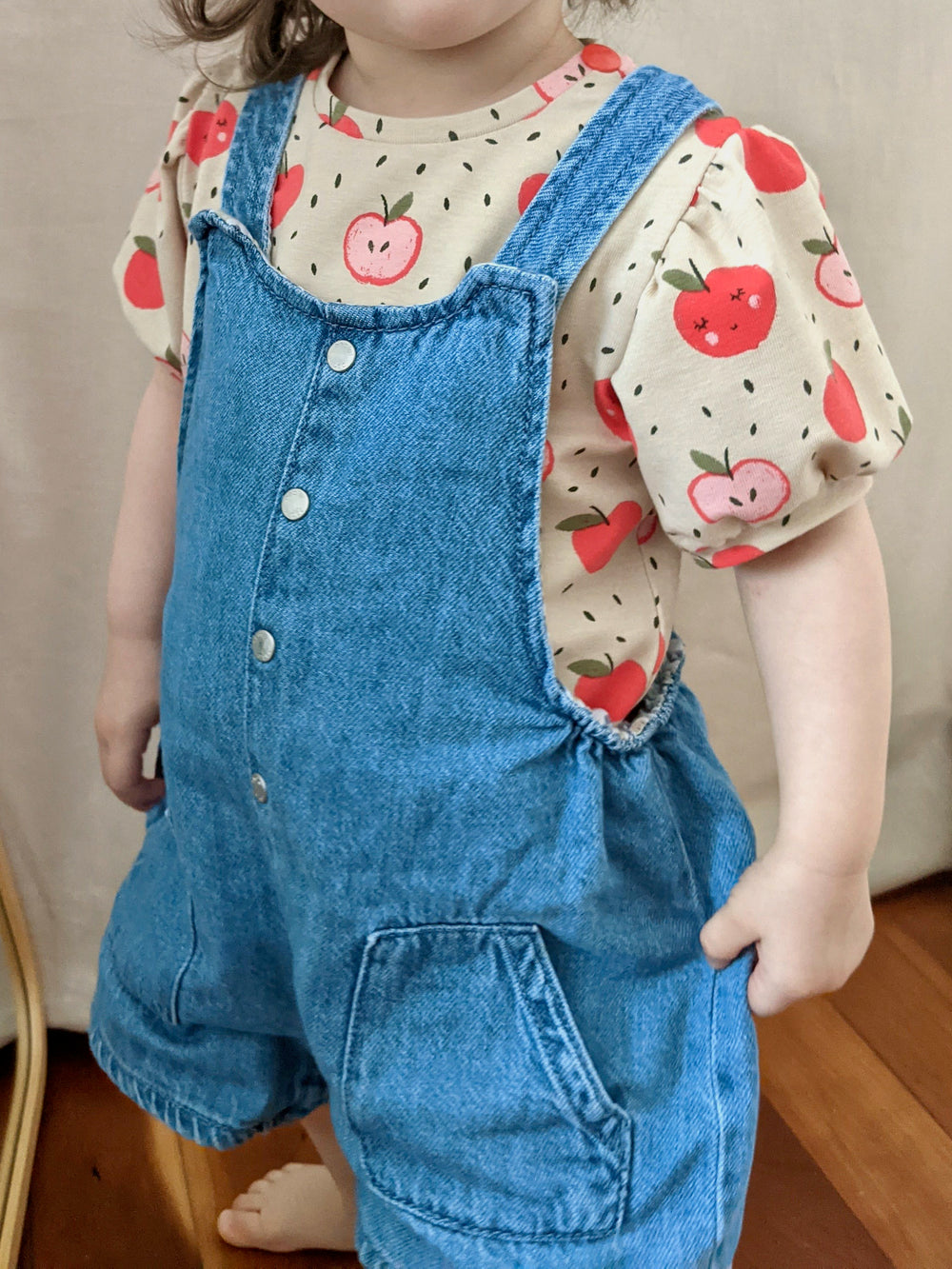 Child wearing the Baby/Child Nuage Mini Balloon Sleeve Shirt sewing pattern from Camimade on The Fold Line. A t-shirt pattern made in light to medium weight knit fabrics, featuring short balloon sleeves, round neck and shoulder opening with snap fasteners