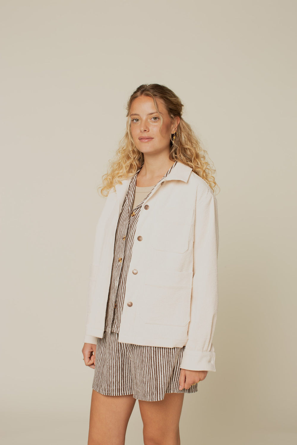 Woman wearing the Canvas Jacket sewing pattern from Wardrobe by Me on The Fold Line. A jacket pattern made in cotton, linen or wool fabrics, featuring a boxy fit, two-piece full length sleeves with button cuffs, three front patch pockets, shirt collar, bu