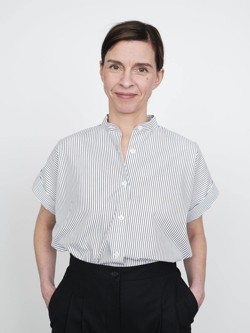Woman wearing the Cap Sleeve Shirt sewing pattern from The Assembly Line on The Fold Line. A shirt pattern made in light to medium weight fabrics such as cotton shirting, featuring a boxy silhouette, stand collar, cap sleeves with turn back cuff and front