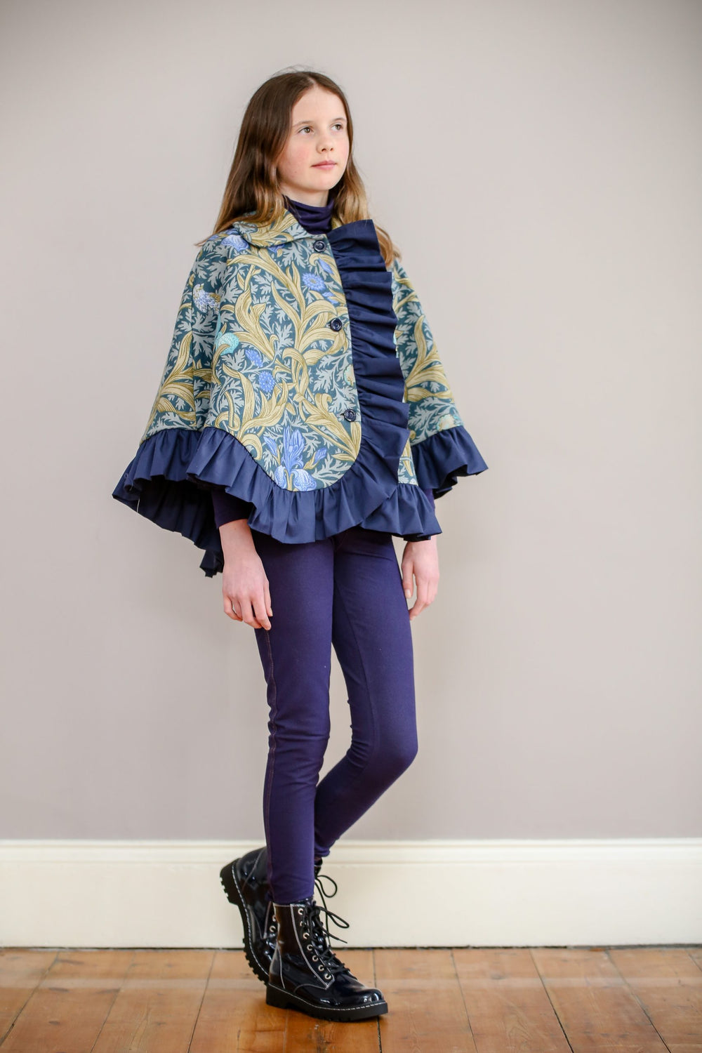 Child wearing the Children's Stornoway Cape sewing pattern by Greyfriars and Grace. A cape pattern made in mid-heavy weight wool, cotton, linen or cotton/linen blend fabric for cape and cotton lining, featuring a front button closure, collar and ruffle he