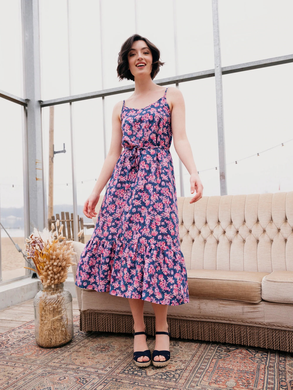 Woman wearing the Chloe Sundress sewing pattern from Atelier Jupe on The Fold Line. A sundress pattern made in viscose, tencel, cotton or linen fabrics, featuring spaghetti shoulder straps, cross back straps, elasticated back, bust darts, tiered hem and m