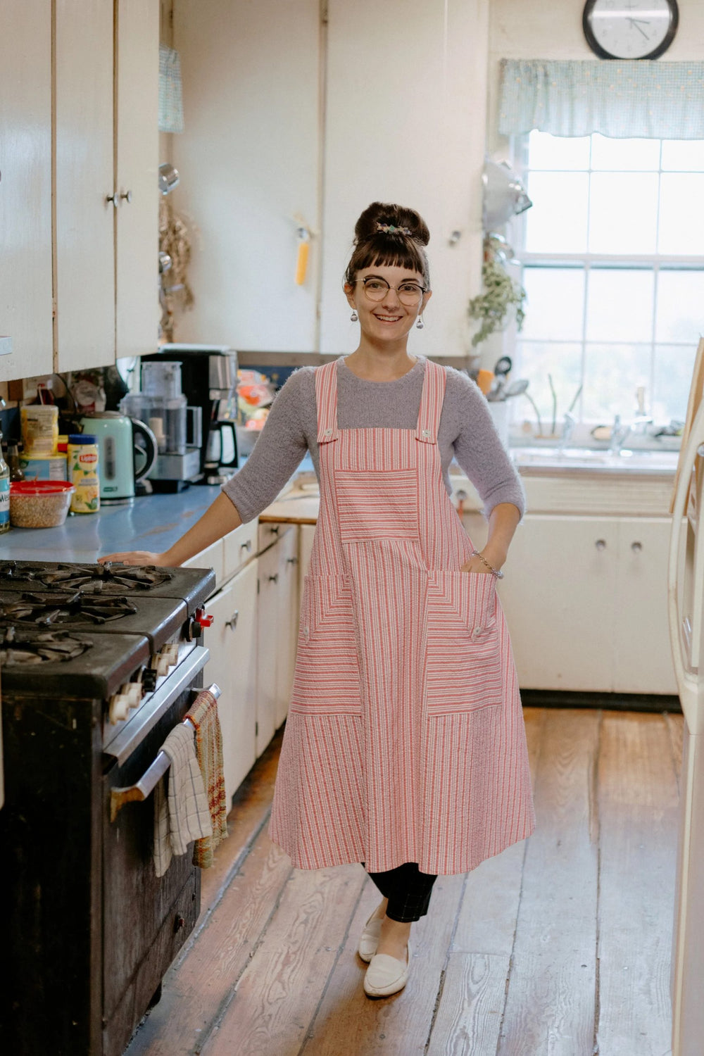 Woman wearing the Cynthia's Cookie Apron sewing pattern from Folkwear on The Fold Line. An Apron pattern made in cotton or linen fabrics, featuring straps that cross over at the back and button at the bib, bib pocket, two oversized patch pockets and A-lin