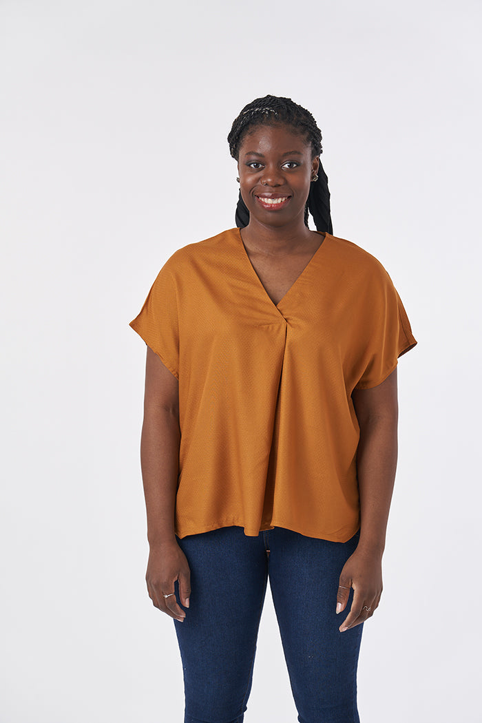 Woman wearing the Cora Top sewing pattern from Sew Over It on The Fold Line. A top pattern made in rayon, viscose or crepe fabrics, featuring a V-neckline with front pleat detail, back pleat grown-on short sleeves, and high-low hem with shallow angled sid