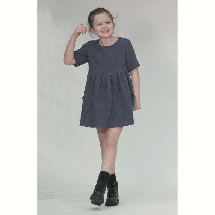 Child wearing the Indi Dress sewing pattern from Pattern Paper Scissors on The Fold Line. A dress pattern made in cotton, viscose, denim, double gauze, linen or crepe fabrics, featuring a relaxed fit, round neck, short sleeves, patch pockets, raised waist