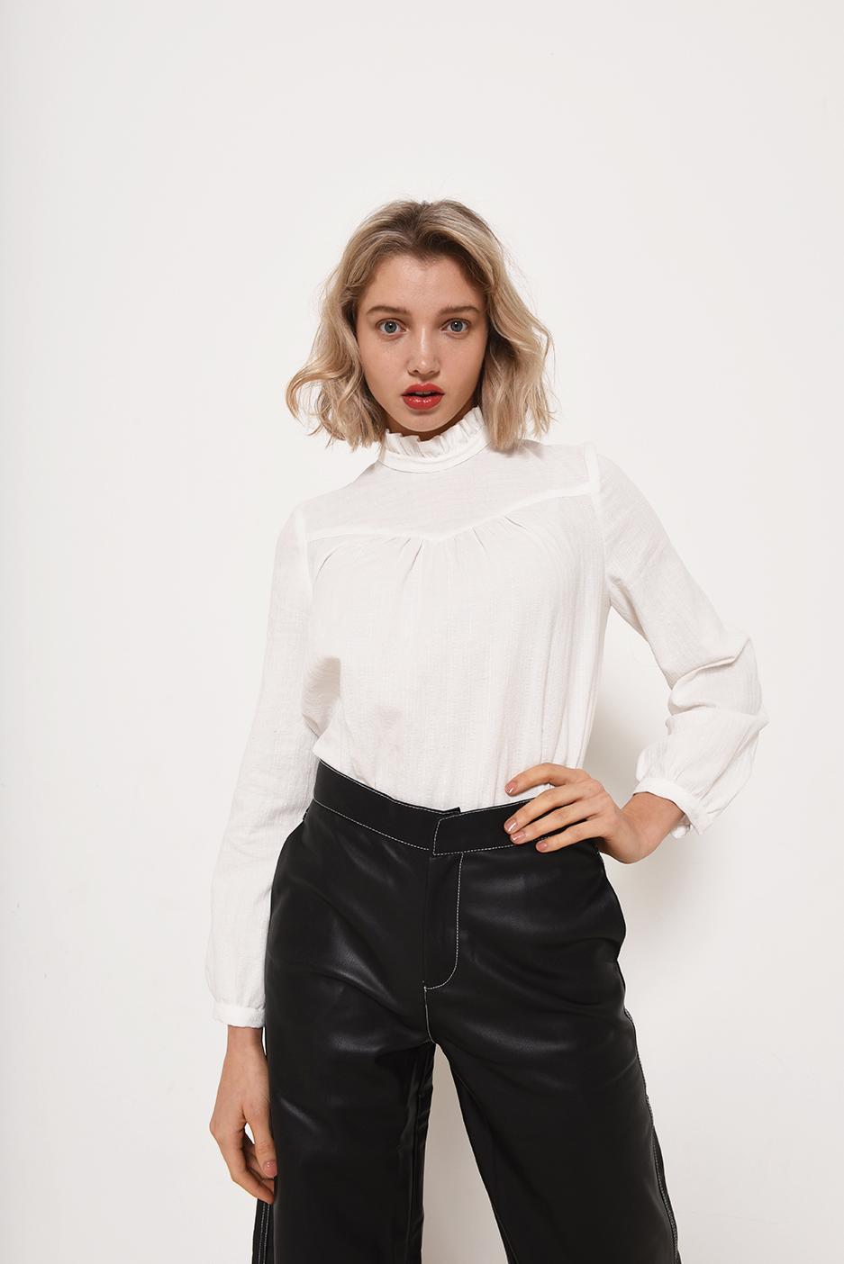 Woman wearing the Victoria Top sewing pattern from Fibre Mood on The Fold Line. A blouse pattern made in cottons or viscose fabrics, featuring a ruffle collar, front yoke with gathers, long sleeves with cuffs, hook and eye back neck closure, and relaxed f