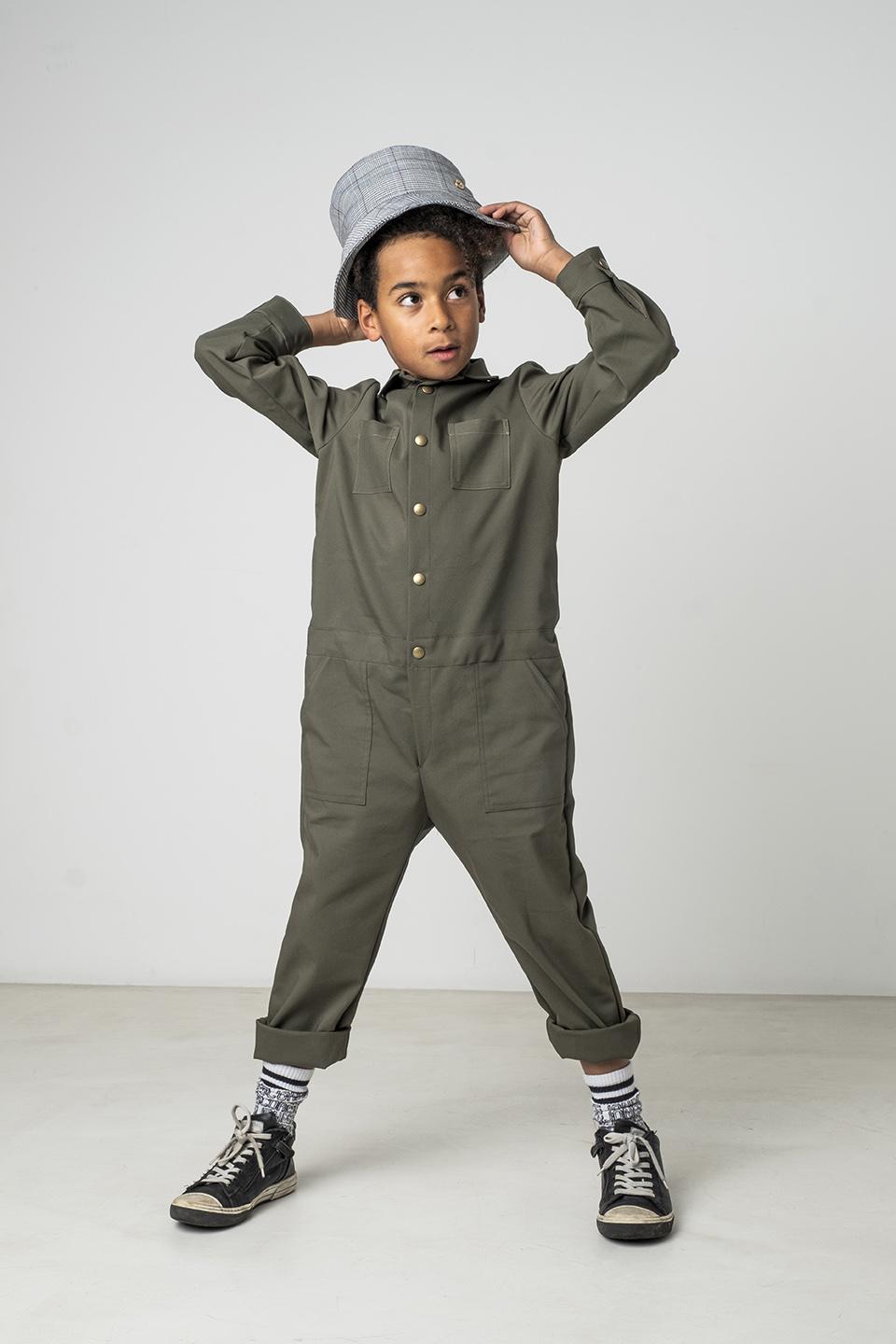 Child wearing the Child/Teen Indigo Jumpsuit sewing pattern from Fibre Mood on The Fold Line. A jumpsuit pattern made in cotton, viscose, wool or denim fabrics, featuring a collar, front button closure, 4 patch pockets, full length sleeves with button cuf