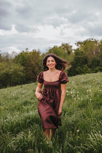 Woman wearing the Daphne Maxi Dress sewing pattern from Sewing Patterns by Masin on The Fold Line. A maxi dress pattern made in cotton, linen, viscose or silk fabrics, featuring an empire waistline, fitted bust, low neckline, short puff sleeves, in-seam p