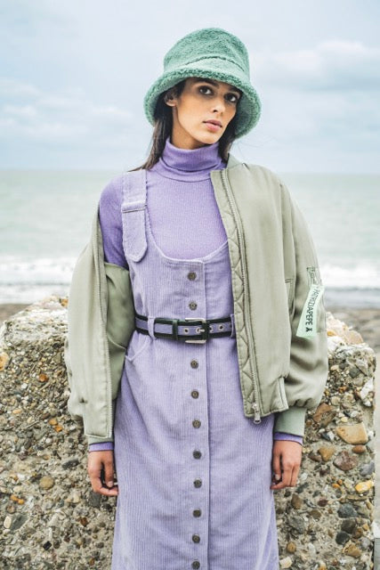Woman wearing the Daria Dress sewing pattern from Fibre Mood on The Fold Line. A dungaree dress pattern made in cotton twill, denim, rib velvet, woollens like houndstooth or Prince of Wales fabrics, featuring front and back pockets, shoulder straps with a