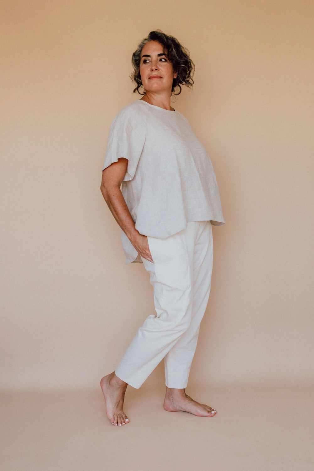 Woman wearing the Darlow Pants sewing pattern from In the Folds on The Fold Line. A trouser pattern made in linen, linen blends, cotton drill/twill, denim or wool fabrics, featuring a cropped length, tapered leg with panel lines and details, sitting on th