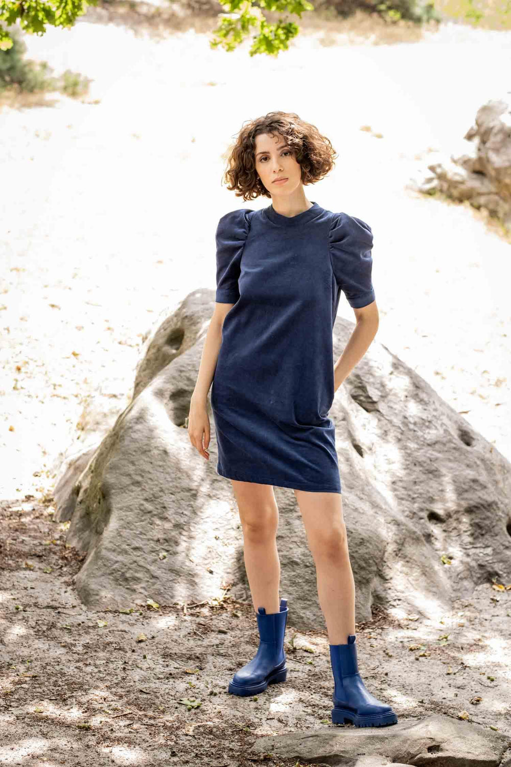 Woman wearing the Dina Dress sewing pattern from Fibre Mood on The Fold Line. A dress pattern made in corduroy, denim, poplin, leather(ette), viscose (crepe), lyocell or satin fabrics, featuring bust darts, gathered short sleeves with deep pleats at the t