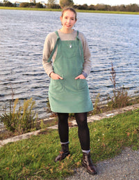 Woman wearing the Dunga Dress sewing pattern from Stitched in Wonderland on The Fold Line. A dungaree dress pattern made in cotton poplin, denim, corduroy, linen, canvas or wool fabrics, featuring patch pockets, chest pocket, adjustable shoulder straps, a