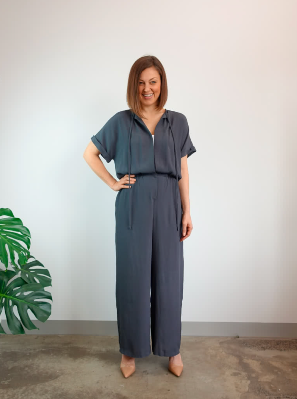 Woman wearing the Eadie Woven Jumpsuit Dress sewing pattern from Style Arc on The Fold Line. A jumpsuit pattern made in silk, crepe or rayon fabrics, featuring an extended shoulder line, turned up sleeve cuffs, elastic waist, front opening, snap closure a