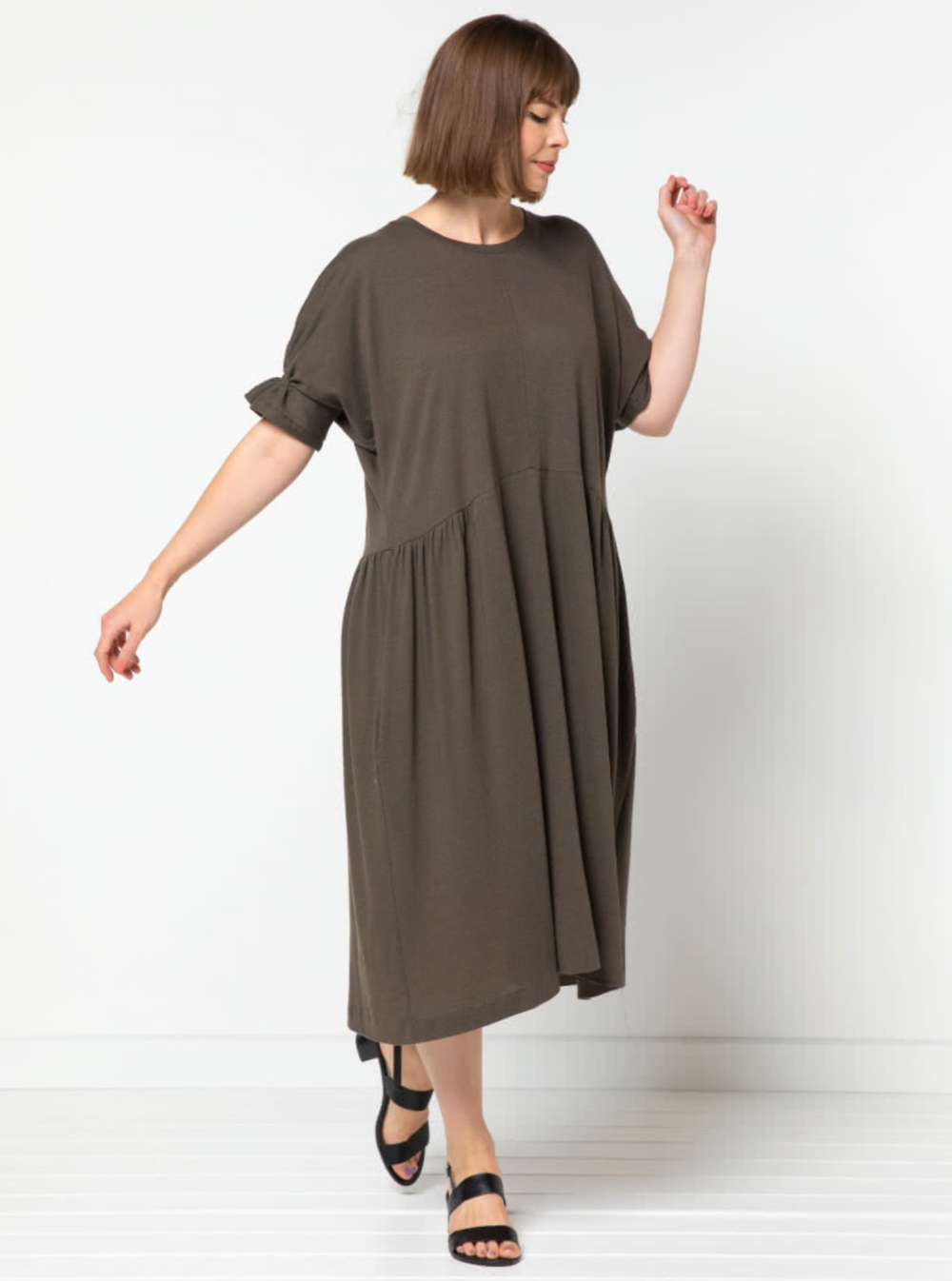 Woman wearing the Eileen Dress sewing pattern from Style Arc on The Fold Line. A dress pattern made in knit or woven fabrics, featuring a relaxed fit, elbow length sleeves with shirring, round neck, gathers at side waist, maxi length and in-seam pockets.