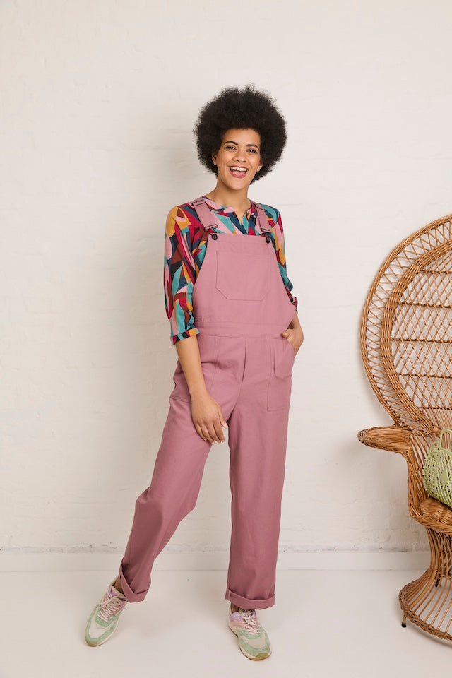 Woman wearing the Elsie Dungarees sewing pattern from Atelier Jupe on The Fold Line. A dungarees pattern made in cotton, denim, corduroy, or linen fabric, featuring topstitched pockets, loose rolled-up trouser legs, a diamond shaped back piece, waistband,
