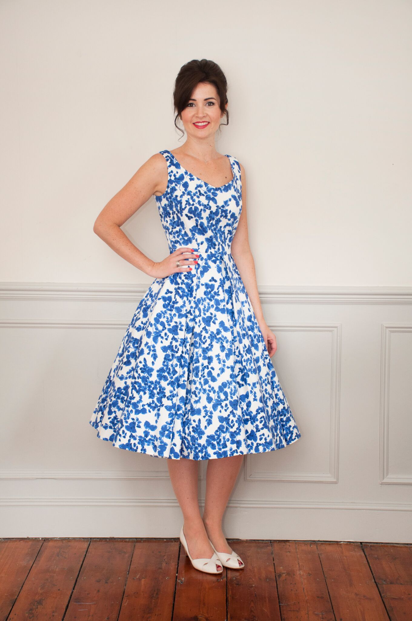 Woman wearing the Elsie Dress sewing pattern from Sew Over It on The Fold Line. A sleeveless dress pattern made in jacquard or stretch cotton fabrics, featuring princess seams, low neckline with a gentle V shape, fitted at the waist, large pleats on the s