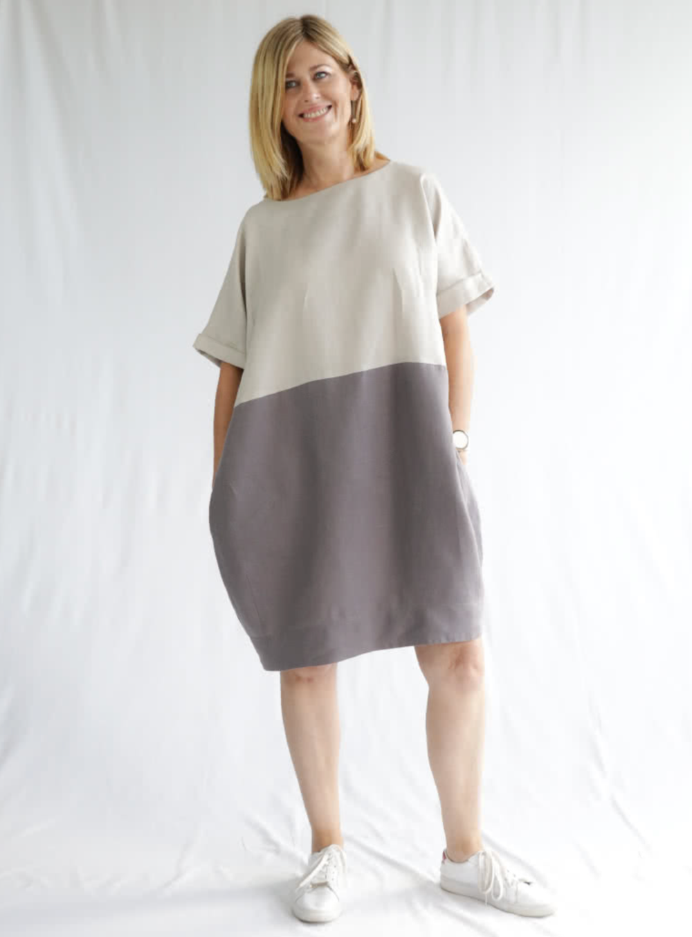 Woman wearing the Eme Dress sewing pattern from Style Arc on The Fold Line. A dress pattern made in silk, rayon, cotton, fine wool or linen fabrics, featuring a loose-fit, cocoon-shape, knee length, boat neck, short sleeves with cuffs and colour blocked.