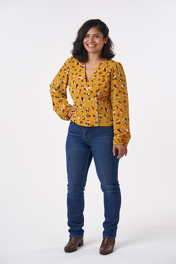 Woman wearing the Esther Blouse sewing pattern from Sew Over It on The Fold Line. A wrap blouse pattern made in rayon, viscose or crepe fabrics, featuring a button front closure, puff shoulders, full length sleeves and V-neckline.