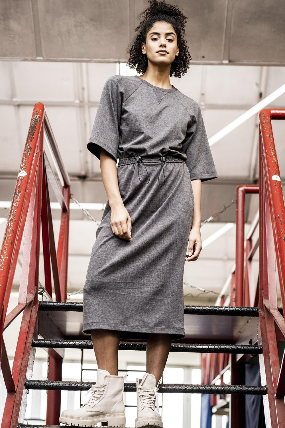 Woman wearing the Joy Dress sewing pattern from Fibre Mood on The Fold Line. A dress pattern made in French terry, interlock or sweatshirt fabrics, featuring a crew neck with neck binding, waistline drawstring and cord stoppers, wide raglan sleeves, relax