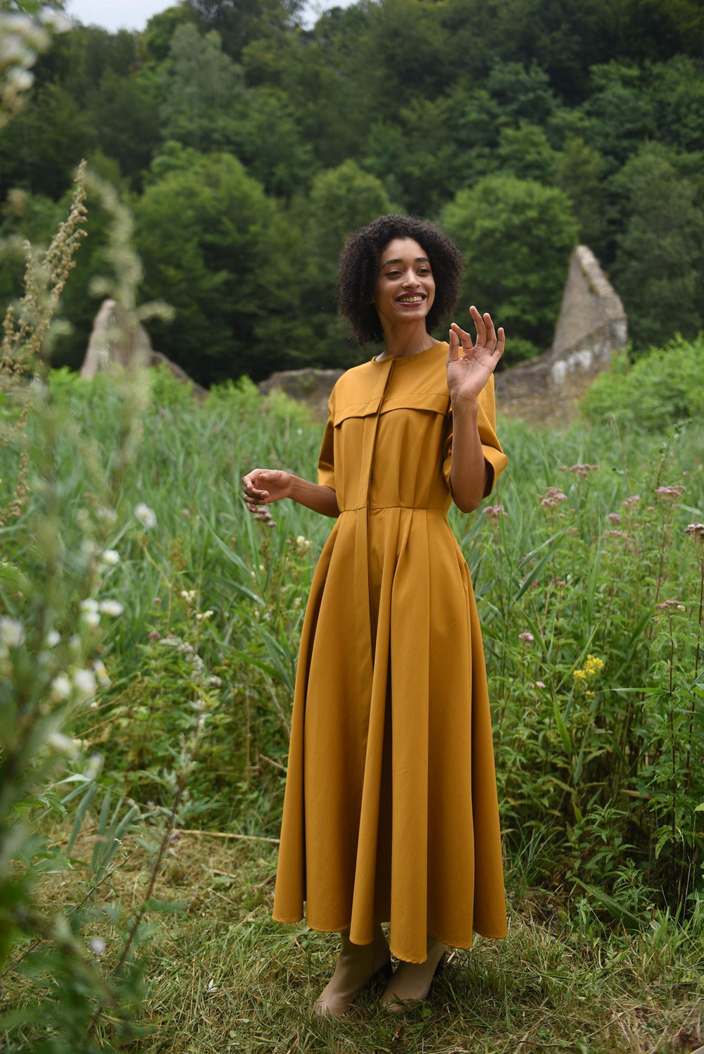 Woman wearing the Faye Dress sewing pattern from Fibre Mood on The Fold Line. A dress pattern made in cotton fabrics, featuring a hidden front button placket, side seam pockets, cuffed short sleeves, circle skirt with front pleats, front and back yoke, ro