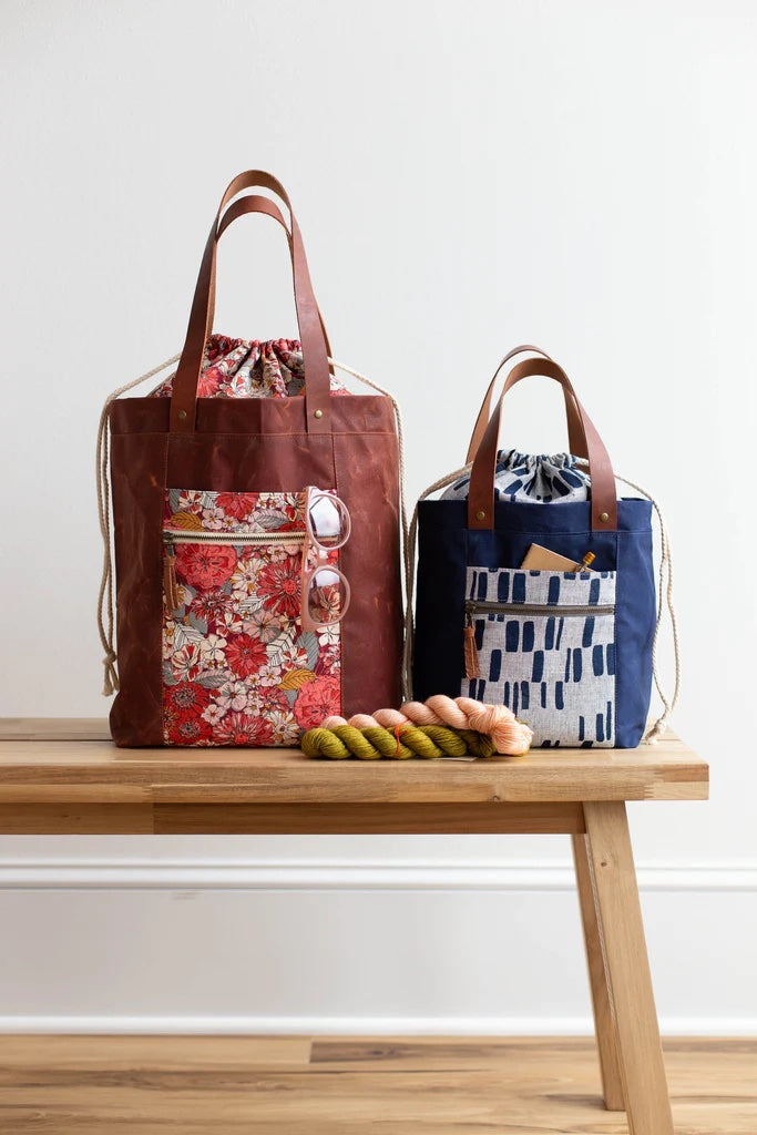 Photo showing the Firefly Totes sewing pattern from Noodlehead on The Fold Line. A tote pattern made in canvas, dry oilskin or waxed canvas fabrics, featuring a large and medium size, drawstring closure, interior slip pocket and front pocket with outer zi