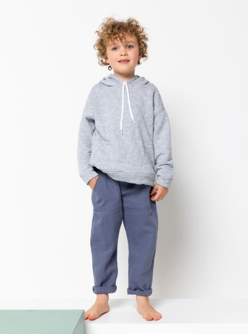 Child wearing the Baby/Child Fitzroy Hoodie sewing pattern from Style Arc on The Fold Line. A hoodie pattern made in ponte, sweater knit or fleece fabrics, featuring dropped shoulders, panelled back, in-seam pockets, hood with drawstring, hem and cuff ban