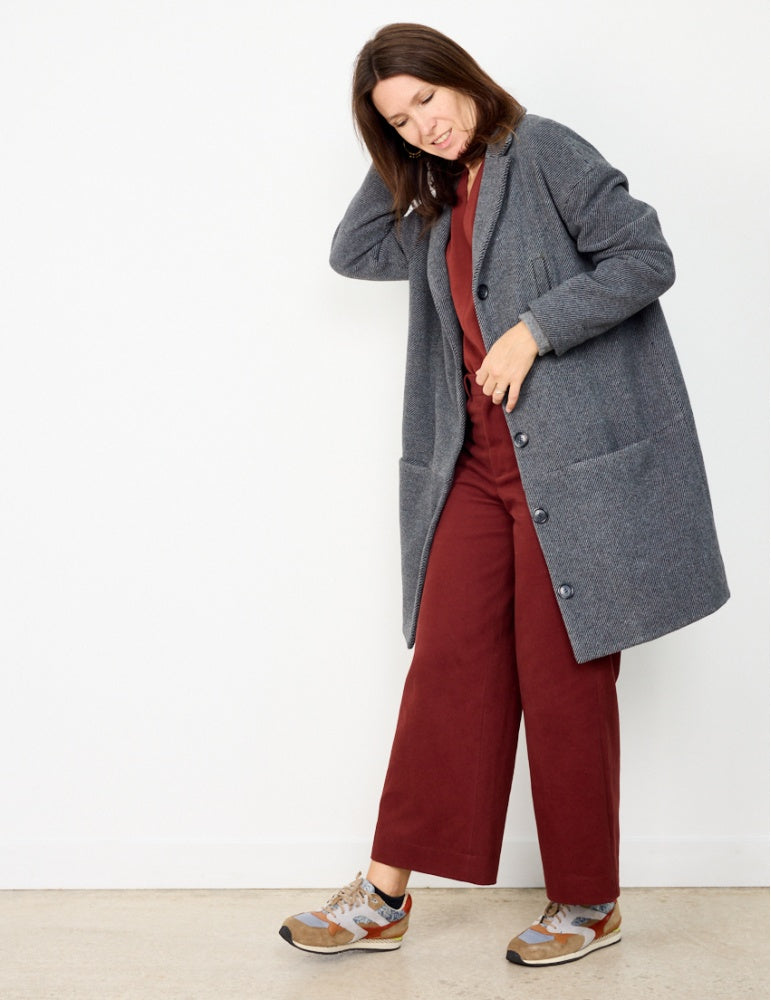 Woman wearing the Flow Coat or Jacket sewing pattern from Atelier Scämmit on The Fold Line. A coat pattern made in woollen or jacquard fabrics, featuring an oversized silhouette, slight round shape, dropped shoulders, tailored collar, pockets, front butto