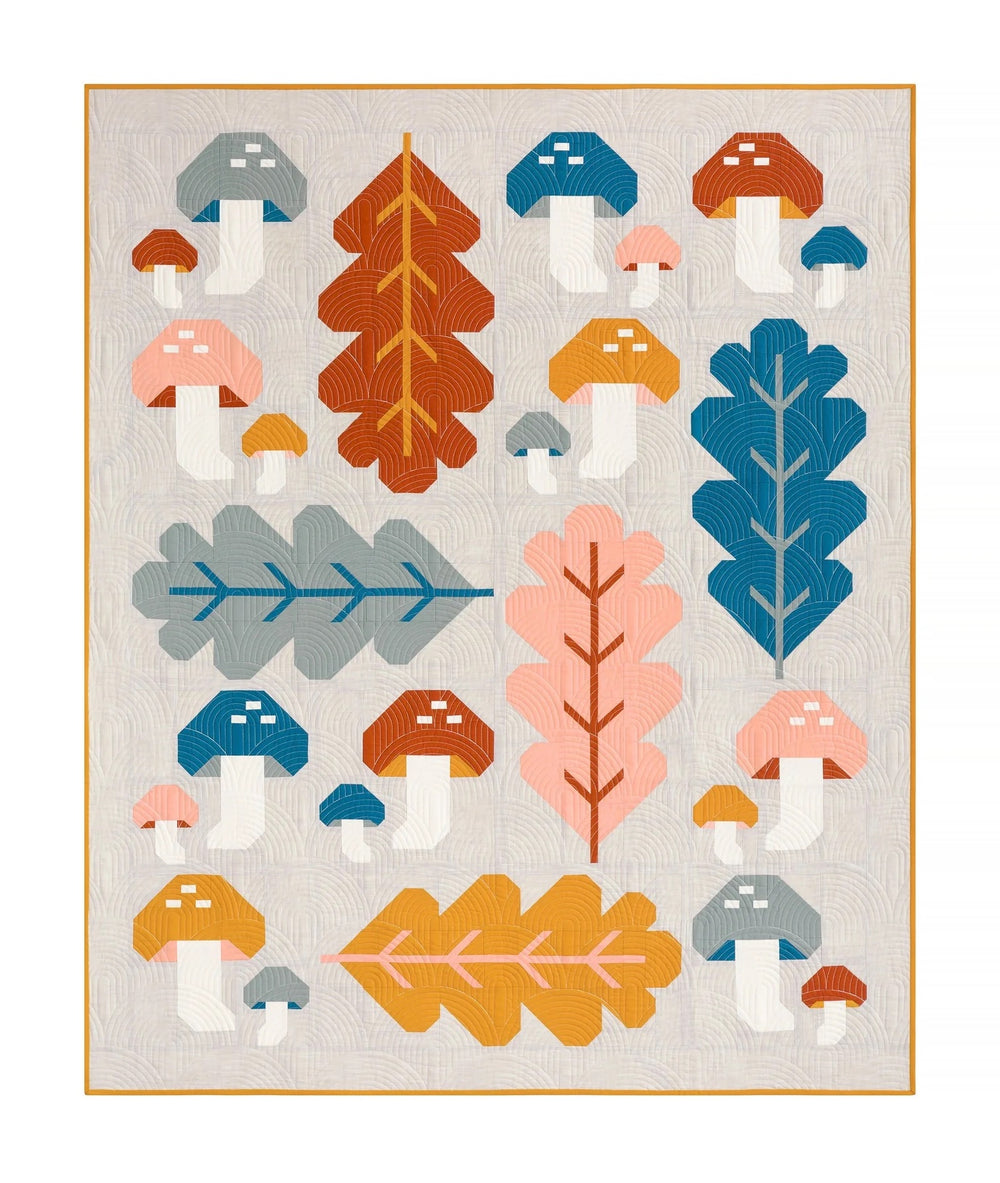 Photo showing the Forest Fungi Quilt sewing pattern from Pen and Paper Patterns on The Fold Line. A quilt pattern made in quilting cotton fabrics, featuring a woodland scene of leaves, toadstools and mushrooms, in blue, brown, mustard and gray colours, a 