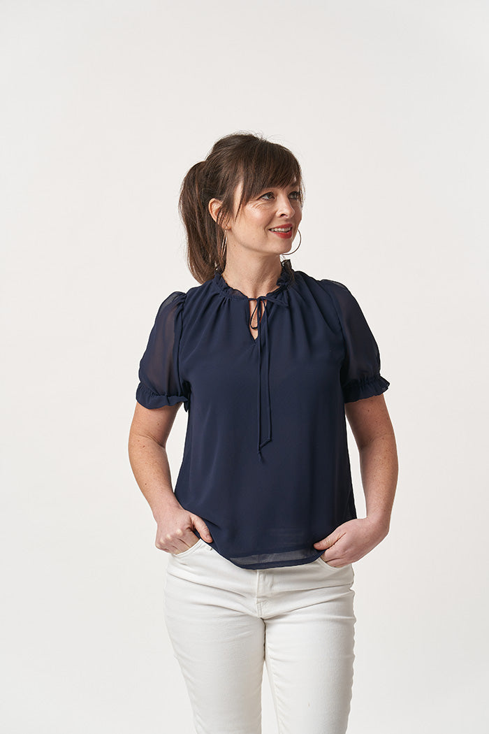 Woman wearing the Freia Blouse sewing pattern from Sew Over It on The Fold Line. A blouse pattern made in chiffon, georgette or fine rayon fabrics, featuring a ruffle collar with Rouleau tie, set-in short puff sleeves gathered with elastic and relaxed fit