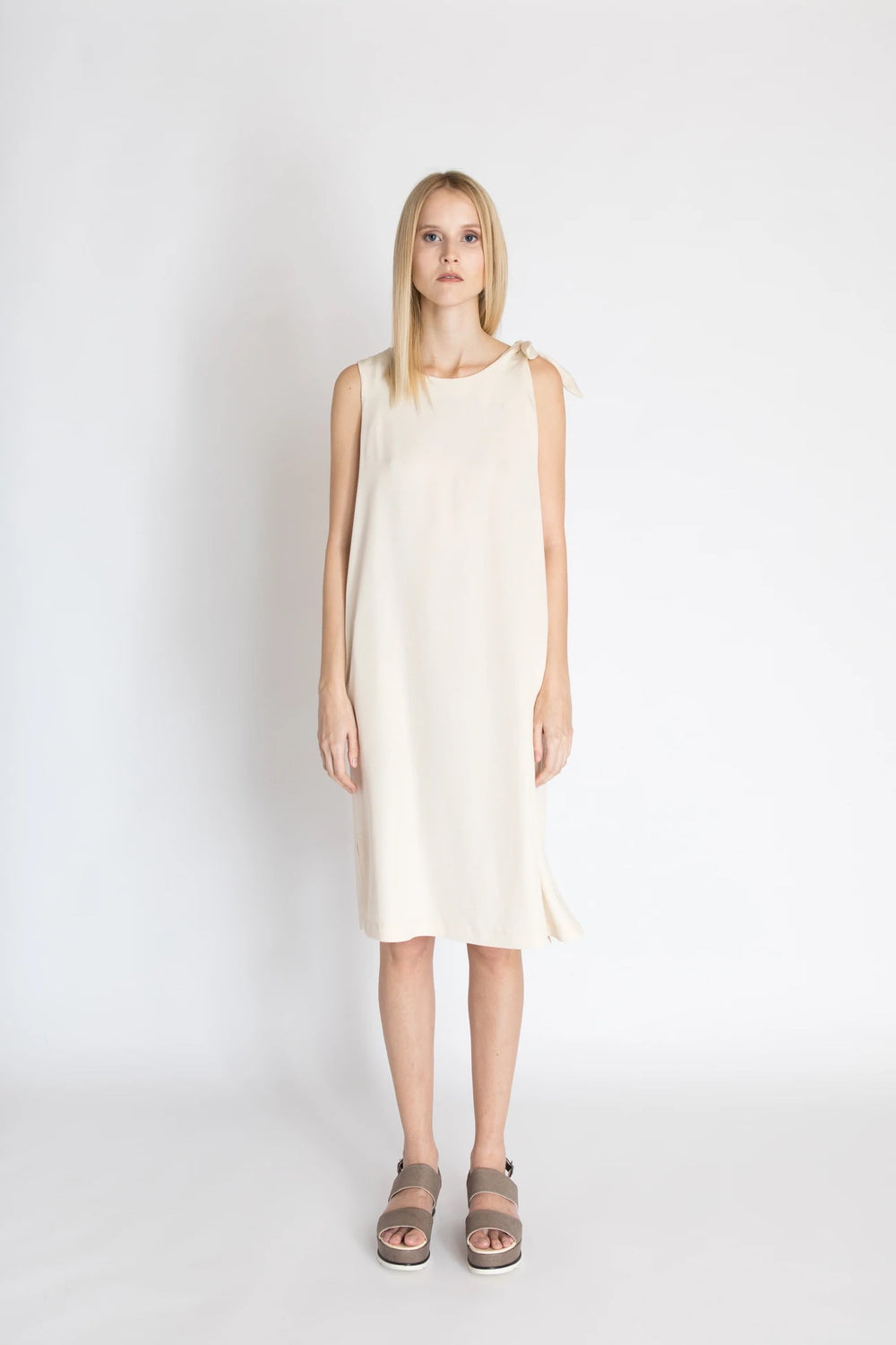 Woman wearing the Freja Knot Dress sewing pattern from Bara Studio on The Fold Line. A sleeveless dress pattern made in cotton, linen or tencel fabrics, featuring a loose-fit, side slits, knot on the left shoulder, in-seam pockets, scoop neckline and knee