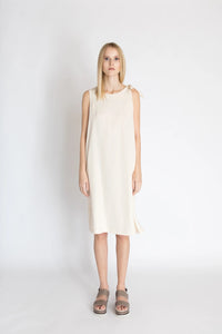 Woman wearing the Freja Knot Dress sewing pattern from Bara Studio on The Fold Line. A sleeveless dress pattern made in cotton, linen or tencel fabrics, featuring a loose-fit, side slits, knot on the left shoulder, in-seam pockets, scoop neckline and knee