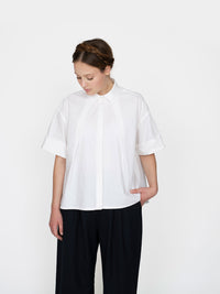 Woman wearing the Front Pleat Shirt sewing pattern from The Assembly Line on The Fold Line. A shirt pattern made in light to medium weight fabrics, featuring a cropped boxy shape, two angled front pleats, back yoke, V-shaped back pleat, short sleeves, and