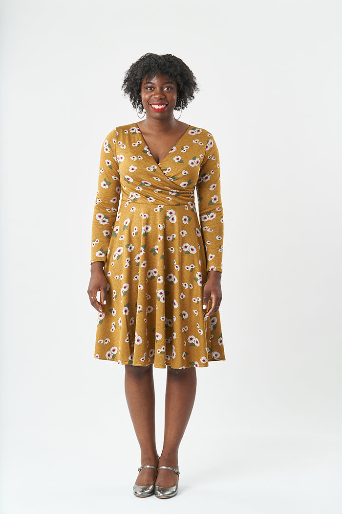 Woman wearing the Georgie Dress sewing pattern from Sew Over It on The Fold Line. A fit and flare knit dress pattern made in light to heavy weight knit fabrics, featuring a V-neck, wrap over bodice with pleats into the side seams, full-length set in sleev