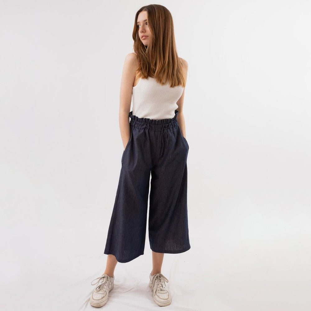 Woman wearing the Georgie Trousers sewing pattern from Fieldwork Patterns on The Fold Line. A culottes pattern made in cotton, cotton mixes, linen, linen mixes or lightweight denim fabrics, featuring wide legs, elastic paper bag waist, in-seam side pocket