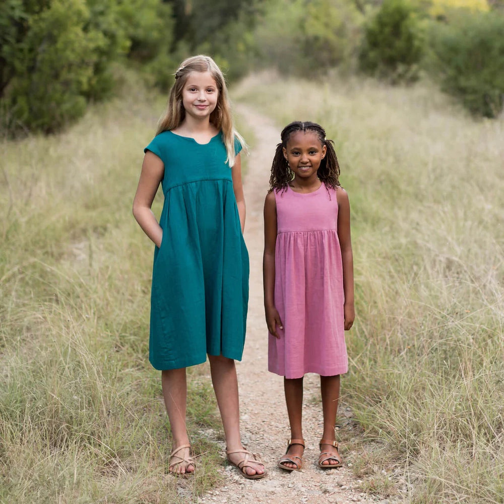 Children wearing the Baby/Child Geranium Dress sewing pattern from Made by Rae on The Fold Line. A dress pattern made in cotton or cotton blend fabrics, featuring faux cap sleeves or sleeveless, high gathered waist, knee length, in-seam pockets, round or 