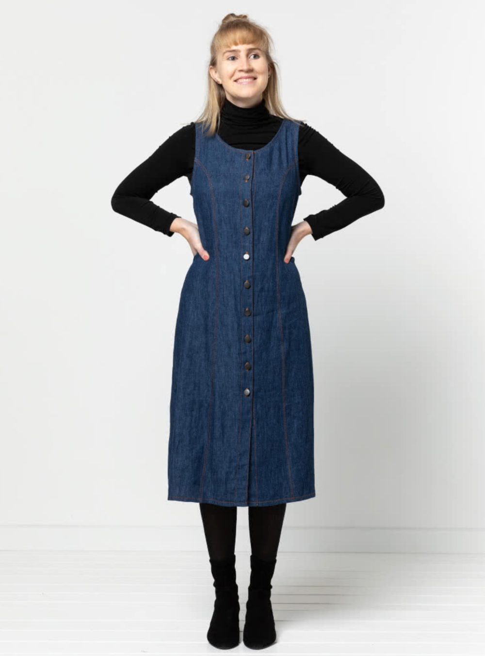 Woman wearing the Geri Dress sewing pattern from Style Arc on The Fold Line. A pinafore dress pattern made in light denim, cord, light wool, or cotton drill fabrics, featuring front and back princess seams, round neck, front button closure and mid-calf le