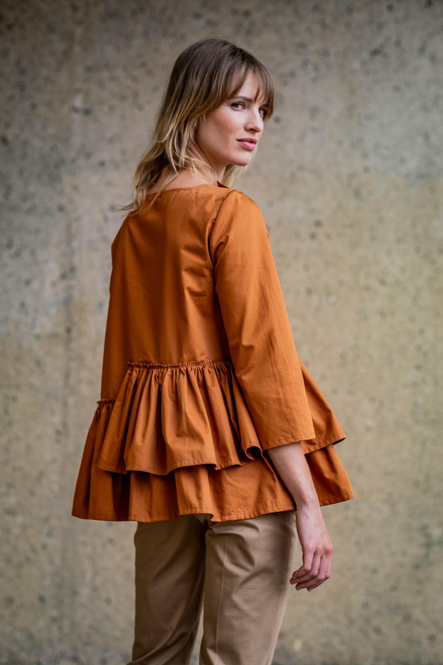 Woman wearing the Ginger Top sewing pattern from Fibre Mood on The Fold Line. A blouse pattern made in poplin, lyocell, chambray, linen, or broderie anglaise fabrics, featuring a concealed snap fastener closure at the shoulder, boat neckline, asymmetrical