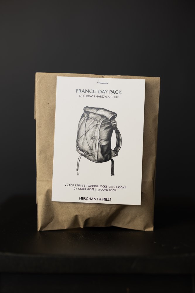 Photo showing the Francli Day Pack from Merchant & Mills on The Fold Line. The kit includes hardware for the bag; 2 x 30 cm ecru/brass zips, 4 x ladder locks, 2 x G hooks, 2 x cord stops, and 1 x cord lock. The metal finish is in Old Brass.